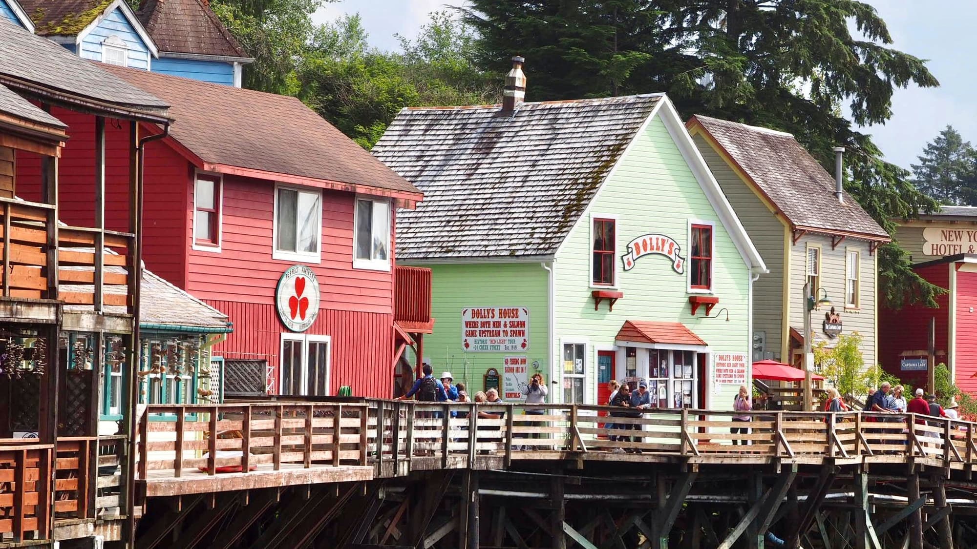 Brightly painted wooden shops along a waterfront boardwalk with people strolling past