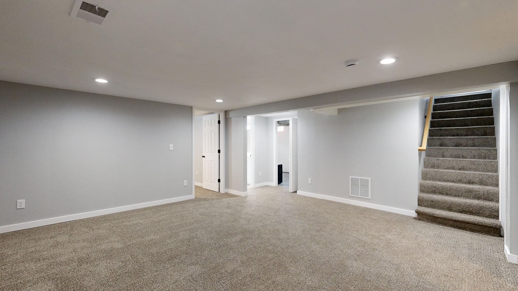 An empty finished basement with carpet and a staircase leading up