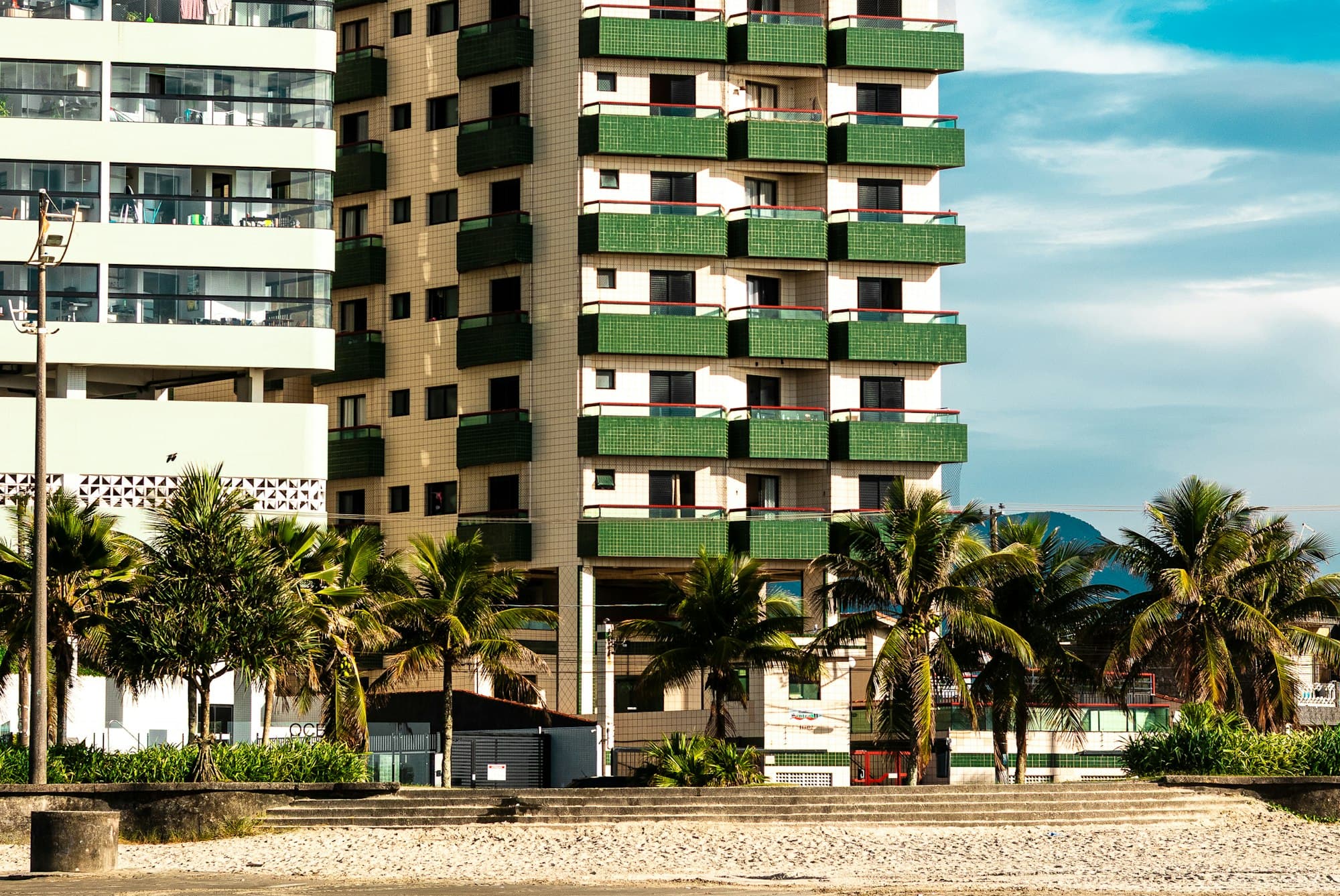 Condo towers with balconied units rising behind palm trees near the beach