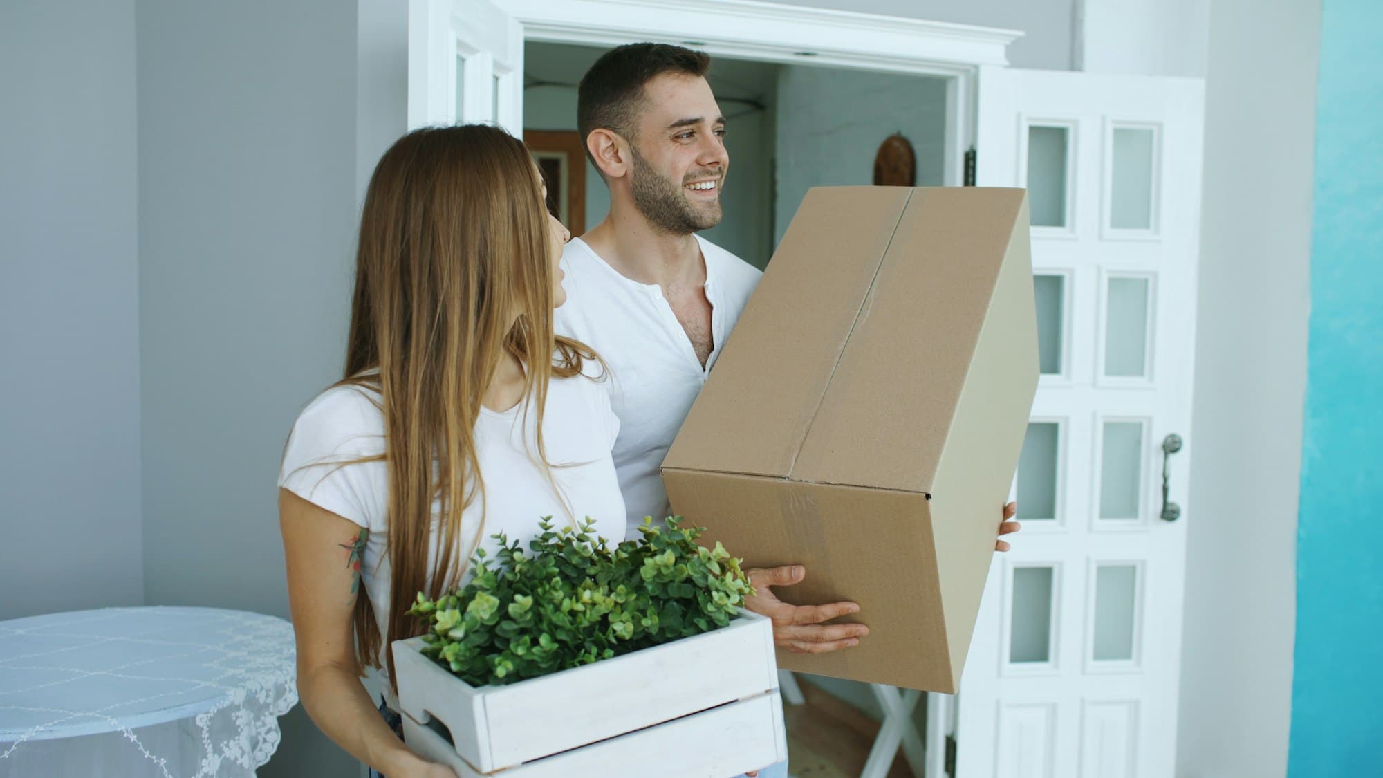 A couple carrying moving boxes through the front door of a new home