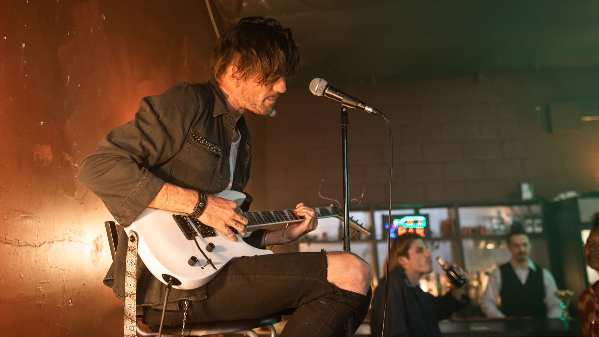 A musician singing into a microphone and playing guitar in a warmly lit bar