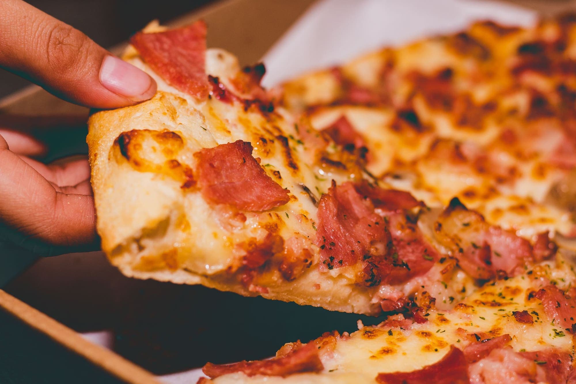 A hand pulling a slice away from a pepperoni pizza, the cheese stretching