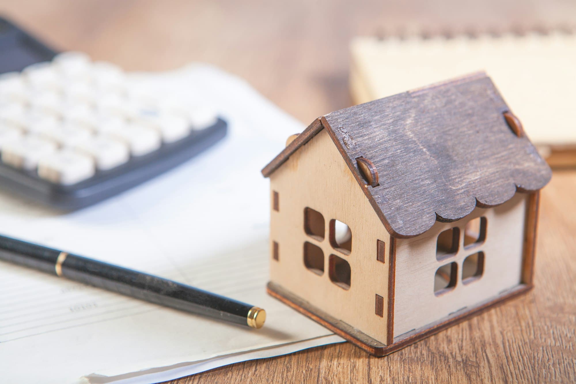 A model house beside a calculator and paperwork on a desk