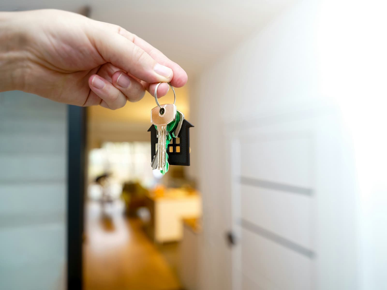 A hand holding house keys in a sunlit doorway