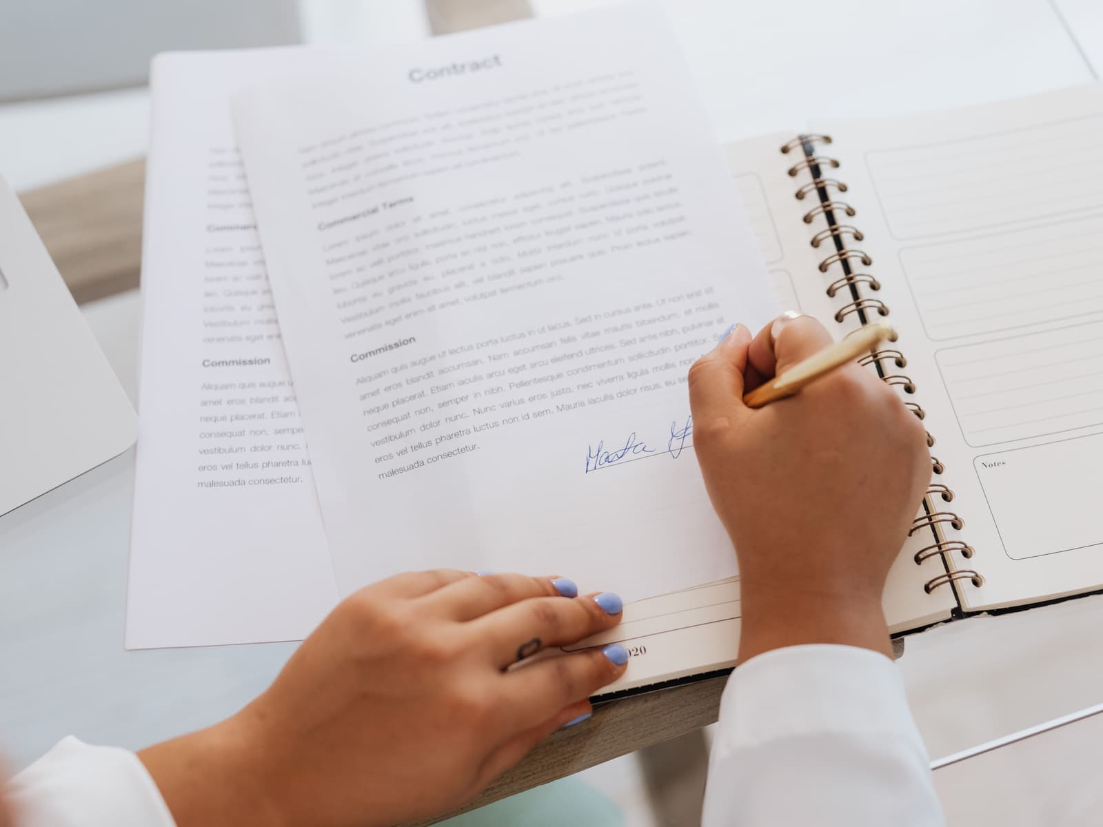 Hands signing a contract beside a notebook on a bright desk