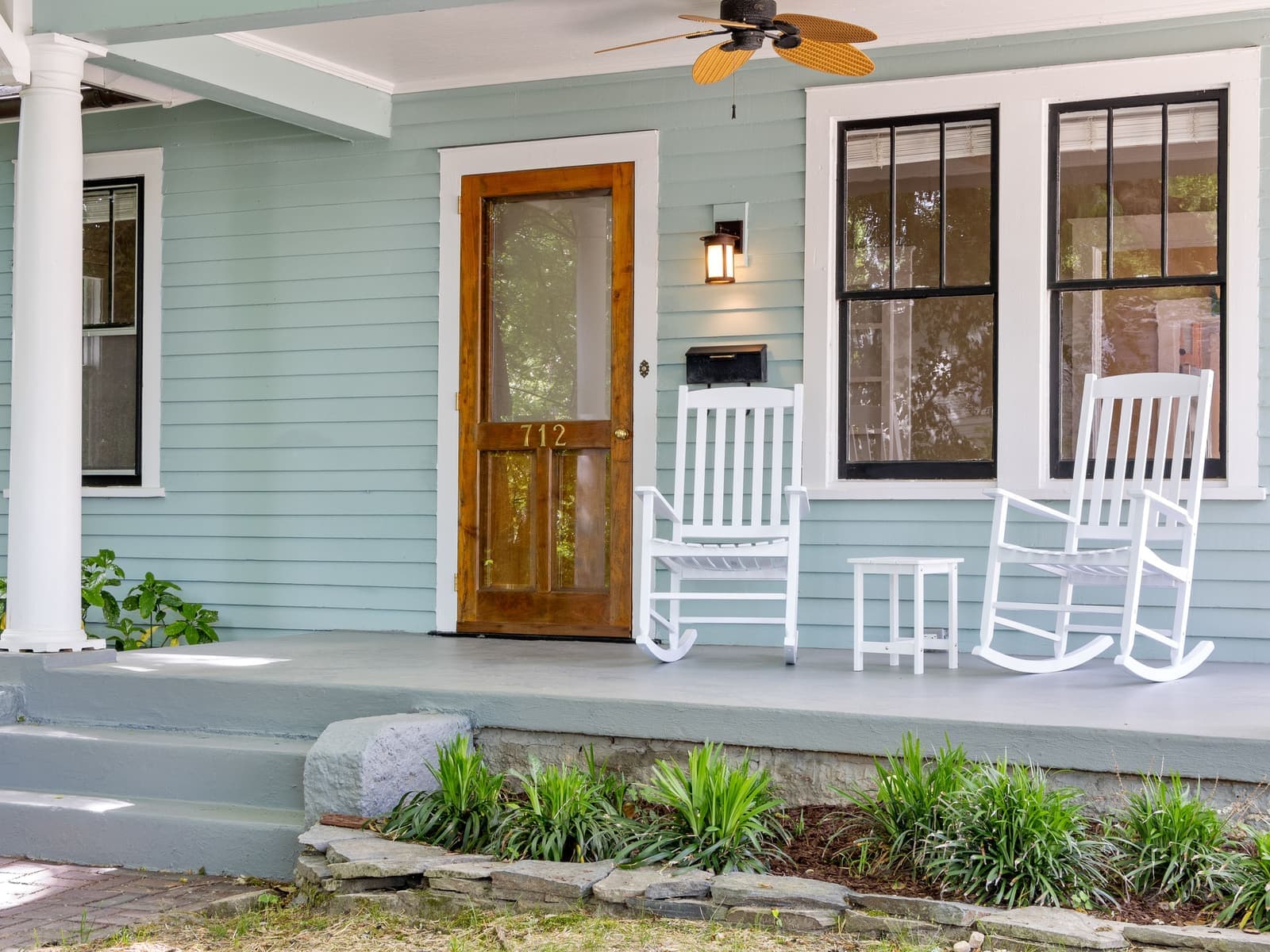 A pale blue-green Southern porch with white rocking chairs and a wooden screen door