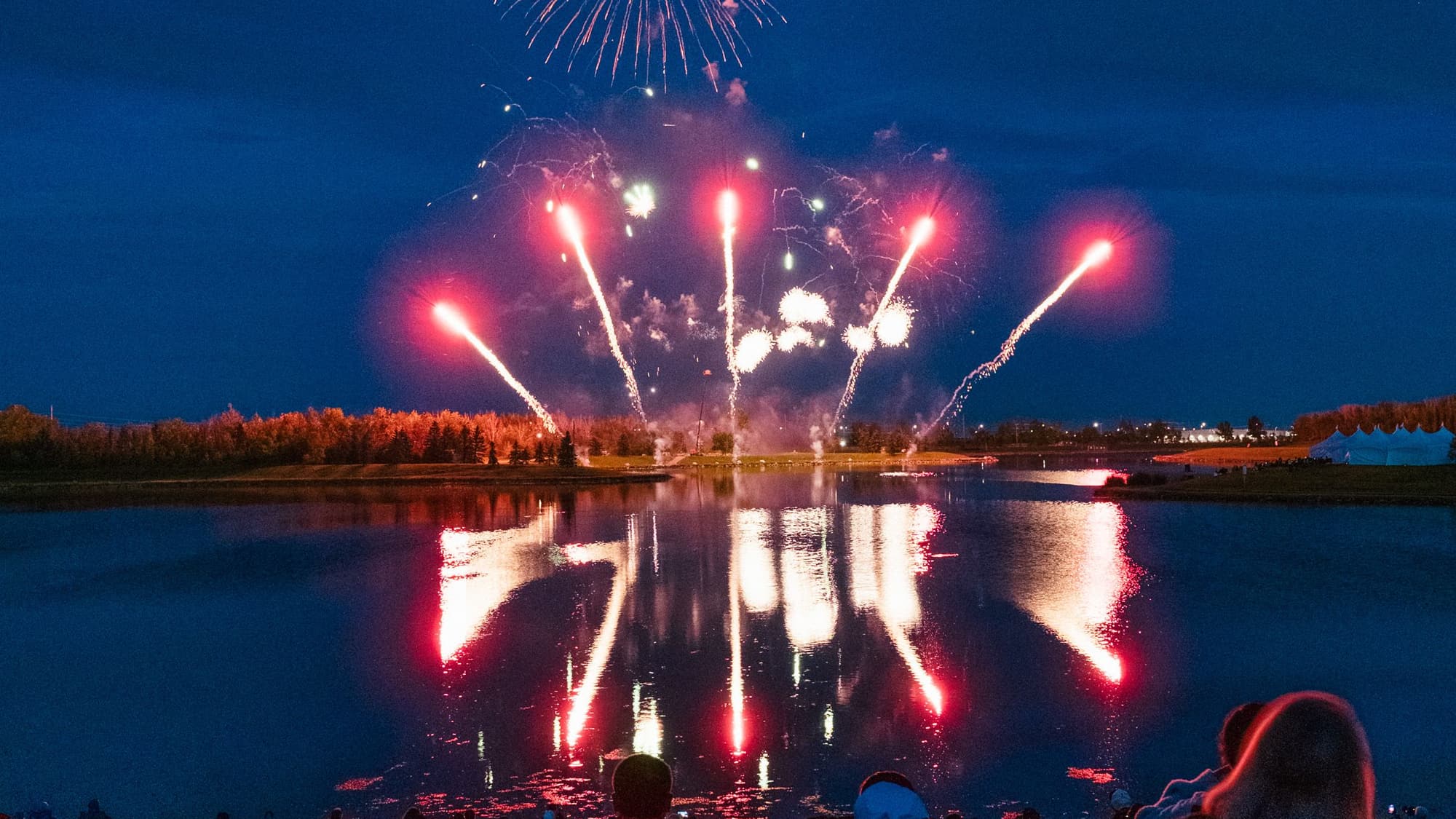 Bright red fireworks bursting over dark water, with their reflections shimmering on the surface