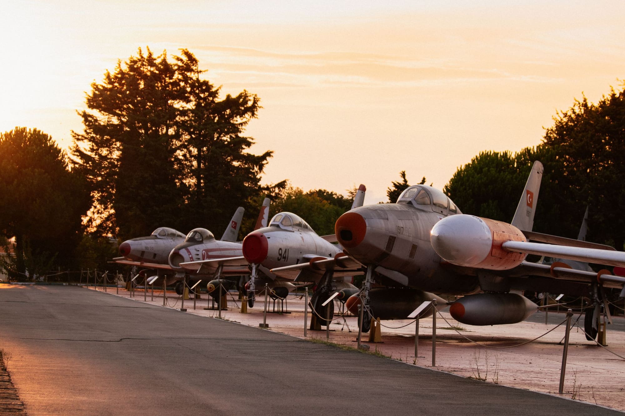 A row of retired fighter jets parked on display along a paved walkway at sunset