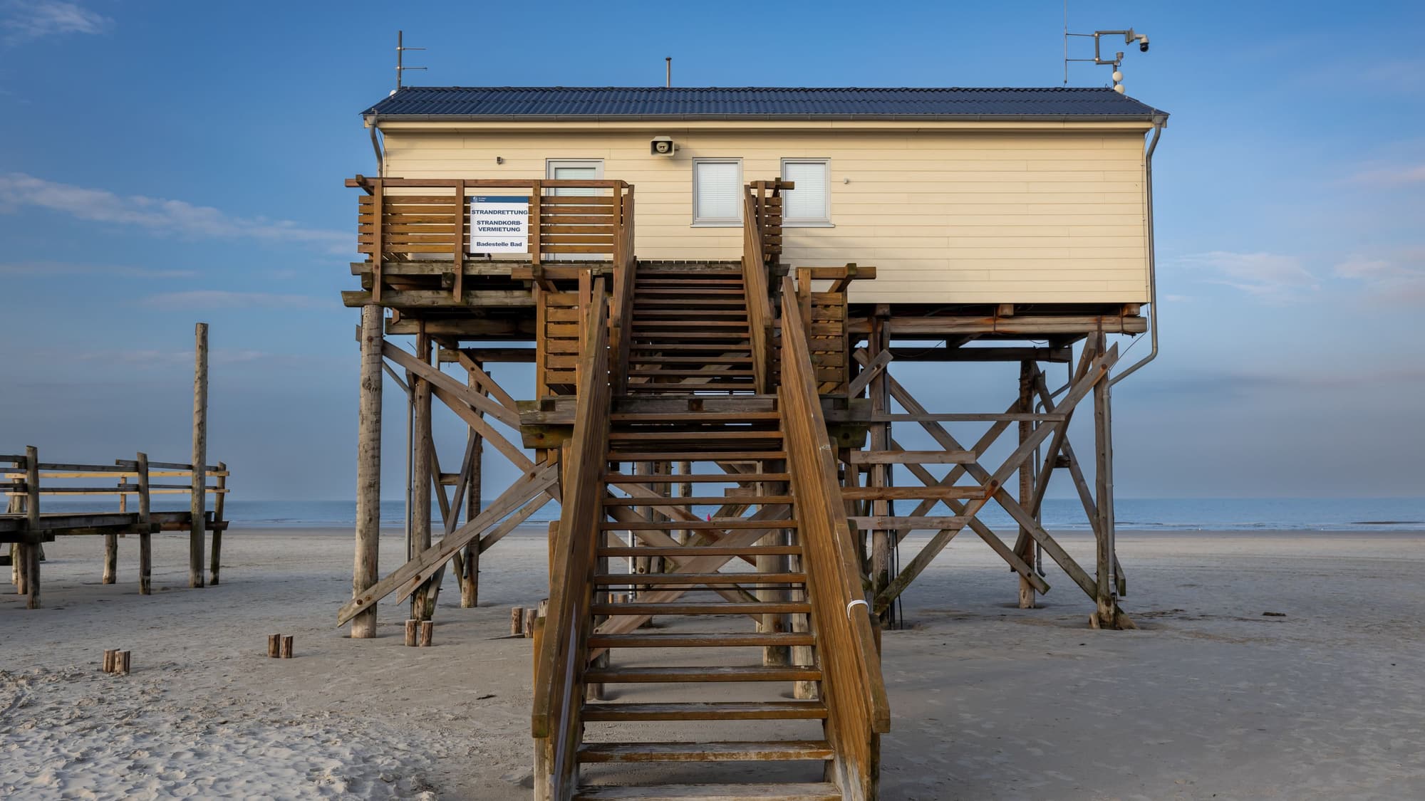 A beach house raised high on wooden pilings with a long staircase leading up from the sand