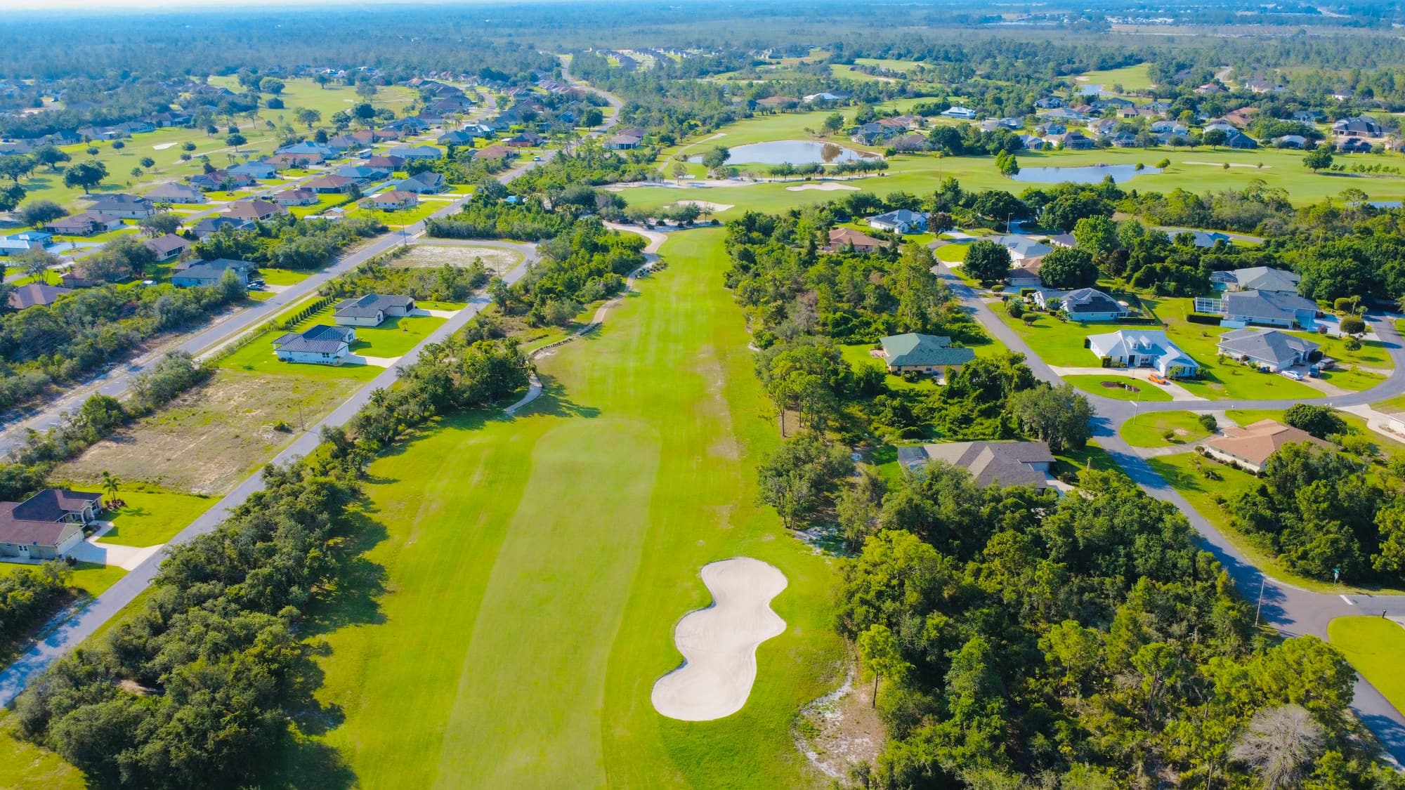 Aerial view of a suburban golf course threading between streets of single-family homes, many backing directly onto the fairways