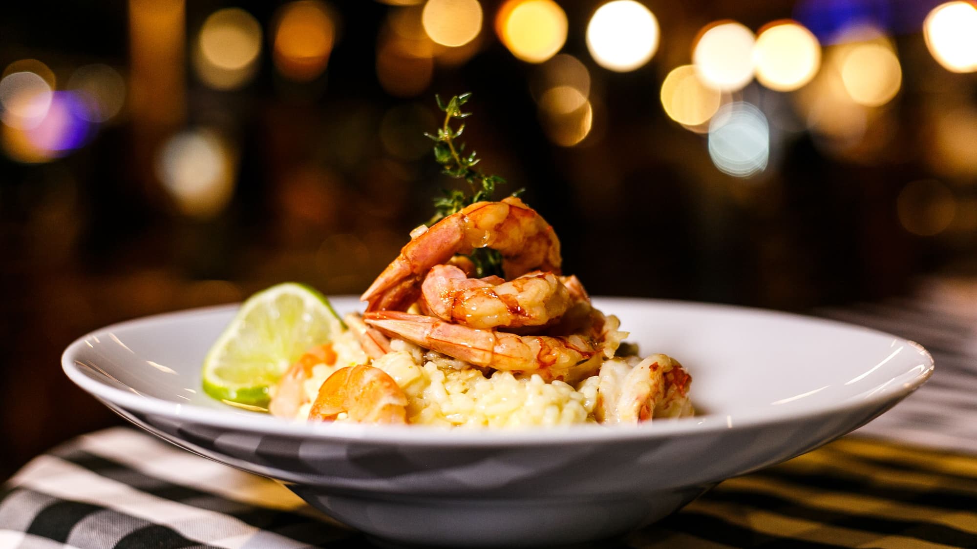 A plated shrimp and grits dish garnished with herbs and lime in a warmly lit restaurant