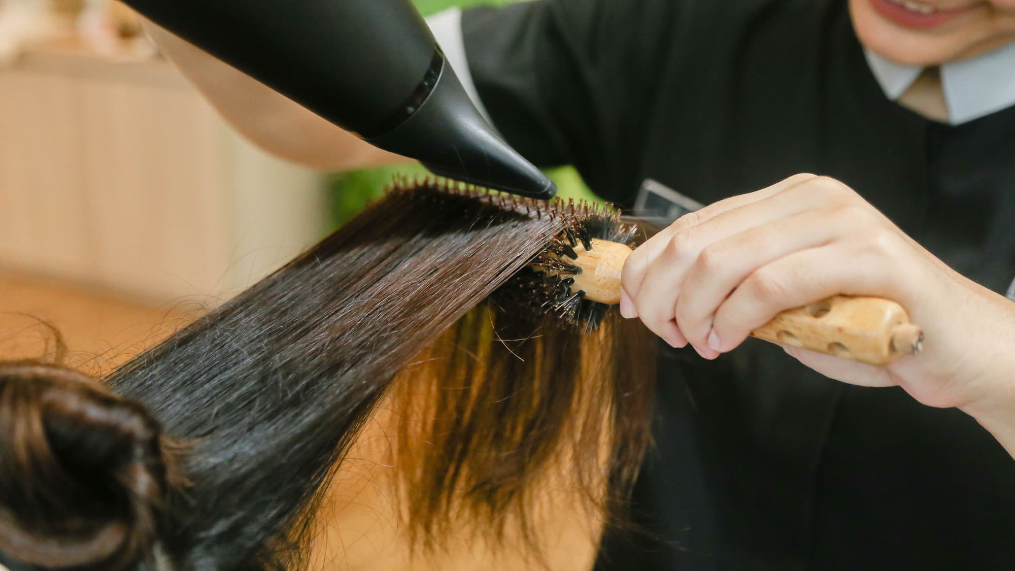 Close-up of someone blow-drying long dark hair straight with a round brush