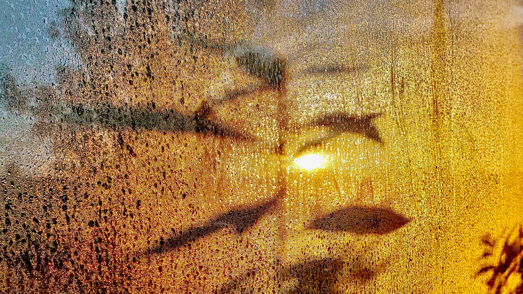 Water droplets and condensation fogging a pane of glass with warm light behind it