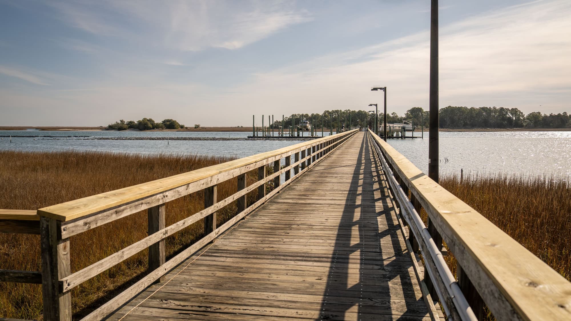 A long wooden pier stretching out over calm water and marsh grass toward a far shoreline