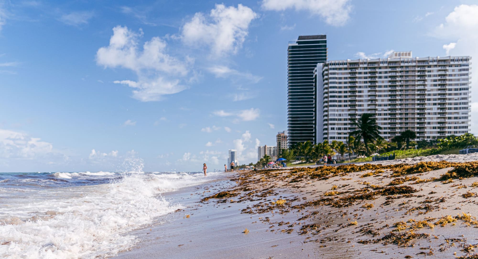 Tall white condominium towers rising behind a beach with waves washing up the sand