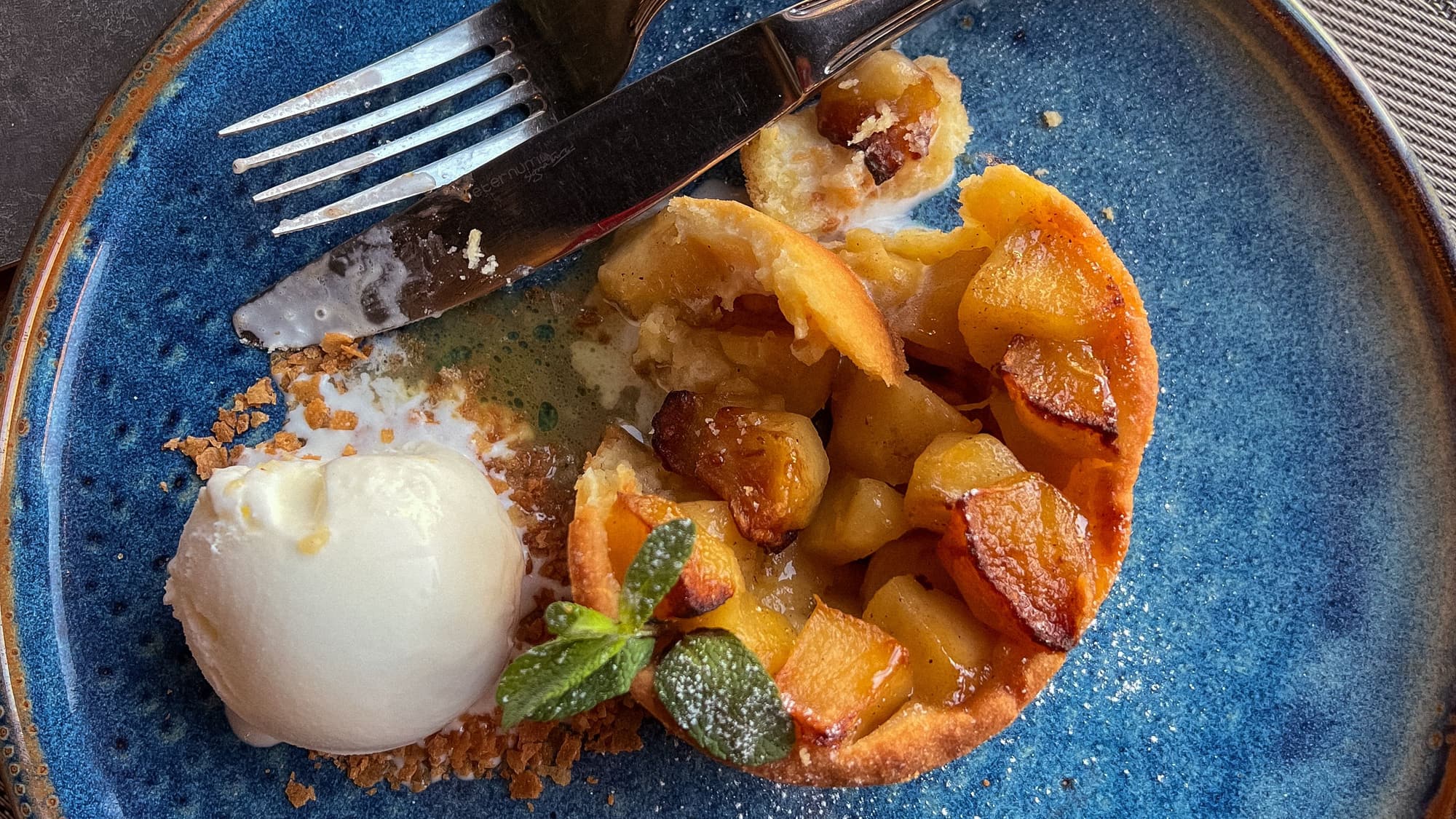 A serving of baked peach dessert with a scoop of vanilla ice cream on a blue plate