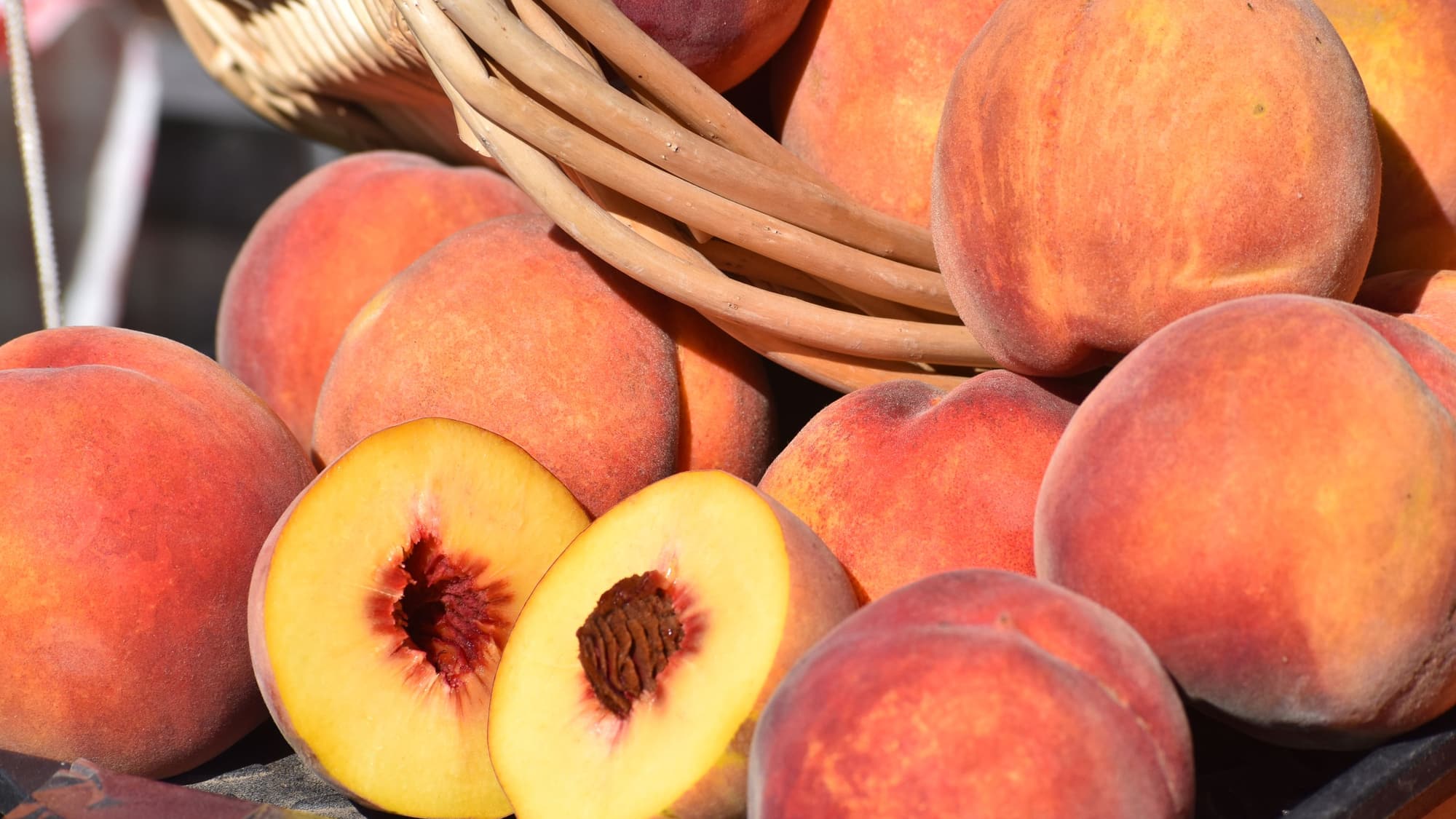 Whole and halved ripe peaches in a basket, with one cut open to show the golden flesh and red pit