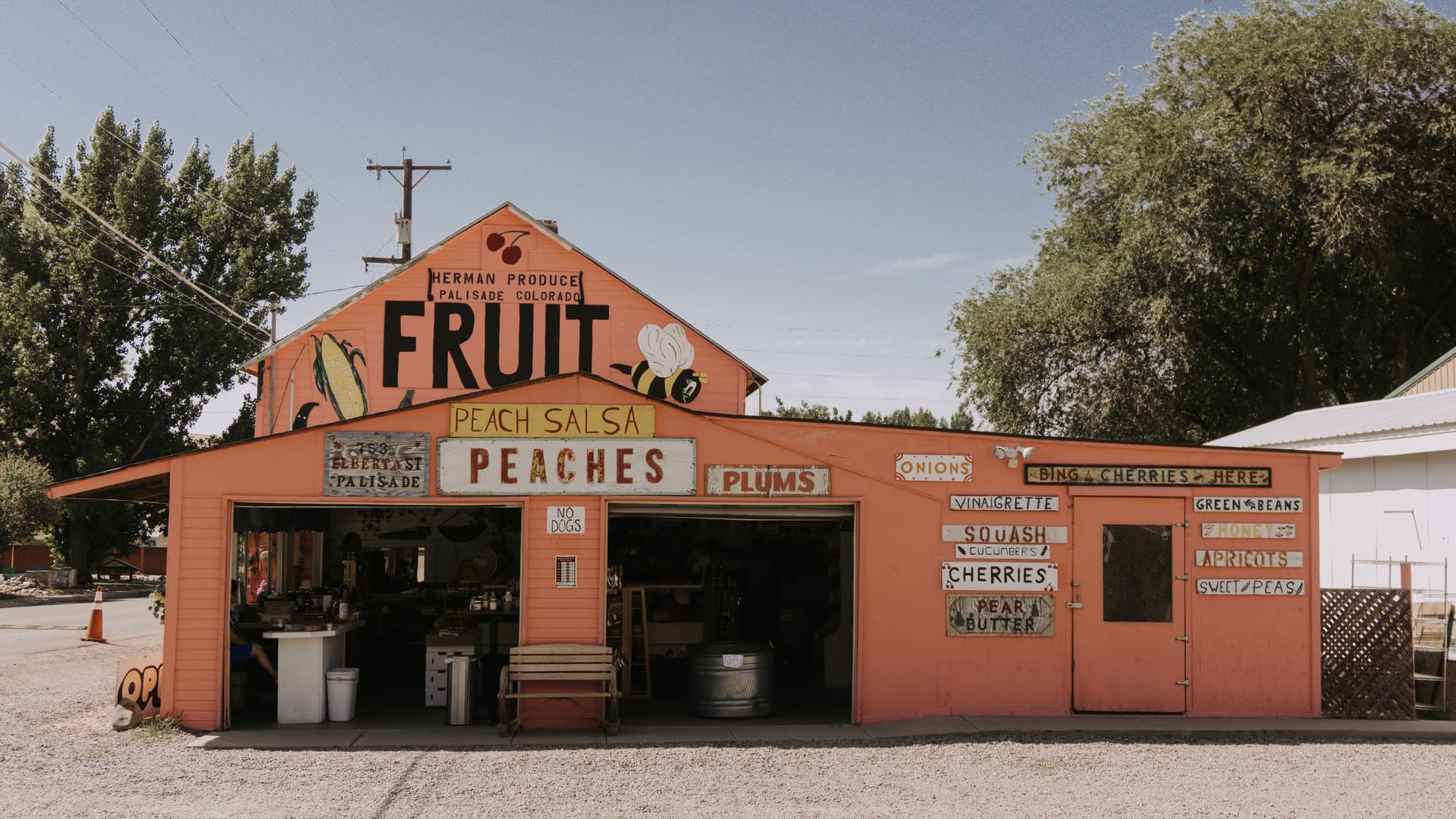 A roadside fruit stand painted peach-orange with big hand-lettered signs for fruit and peaches