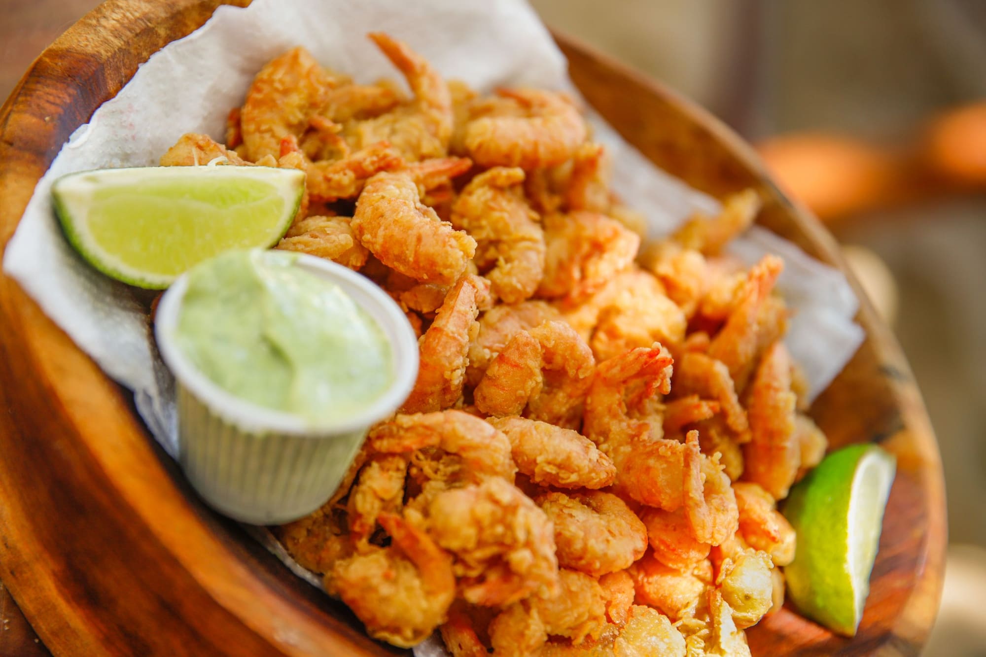 A basket of fried shrimp with lime wedges and a small cup of dipping sauce