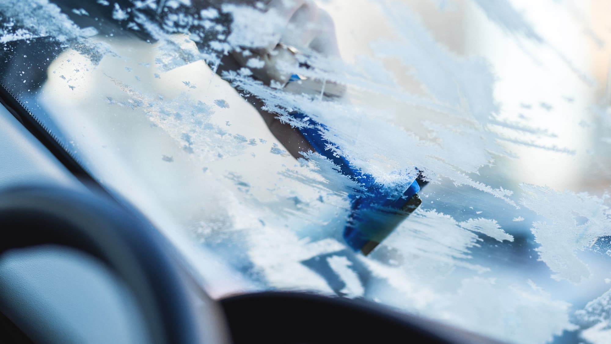 Close-up of a blue ice scraper clearing frost from a car windshield