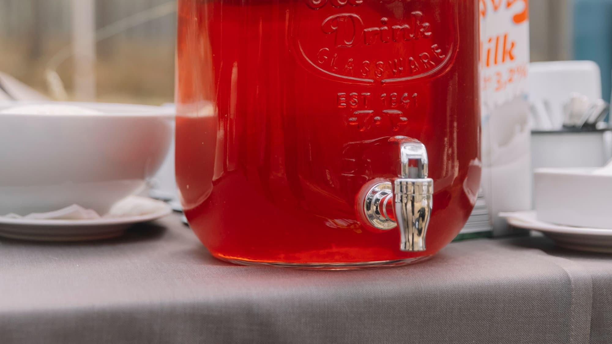 A large glass jar with a spigot filled with deep amber iced tea on a table