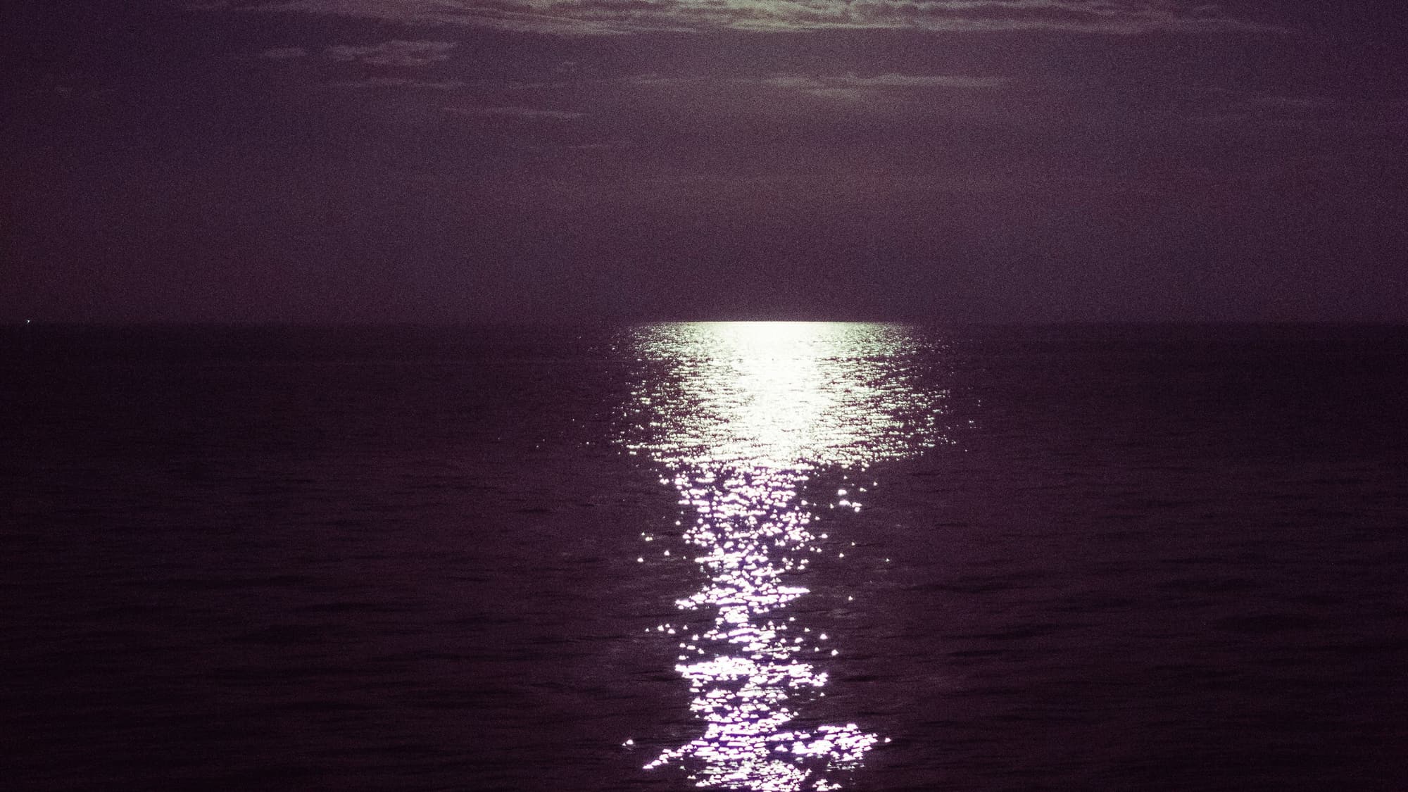 Moonlight reflecting in a bright path across a dark, calm ocean at night
